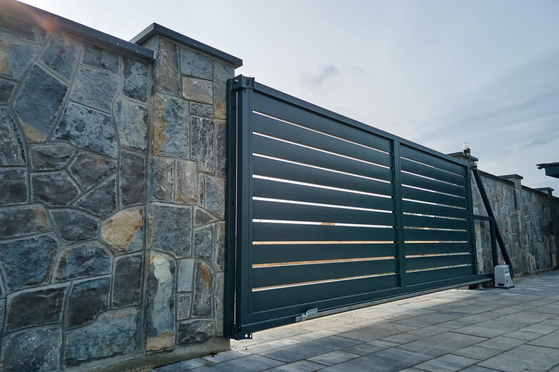 Wide automatic sliding electric gate with remote control installed in high stone fense wall. Security and protection concept.